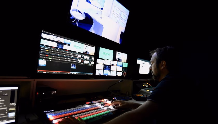 Technicien du Studio Webcast en régie pendant une diffusion en direct, avec mélangeur vidéo et multi-écrans de contrôle