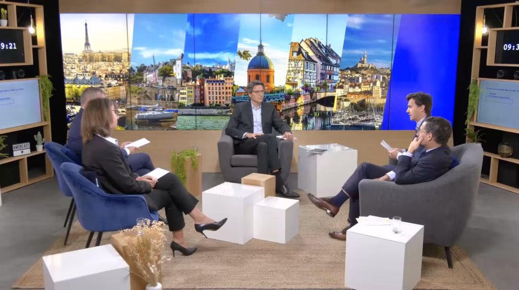 Production en direct au Studio Webcast en configuration talk show avec cinq intervenants, fauteuils gris et bleus, et fond LED panoramique de villes françaises