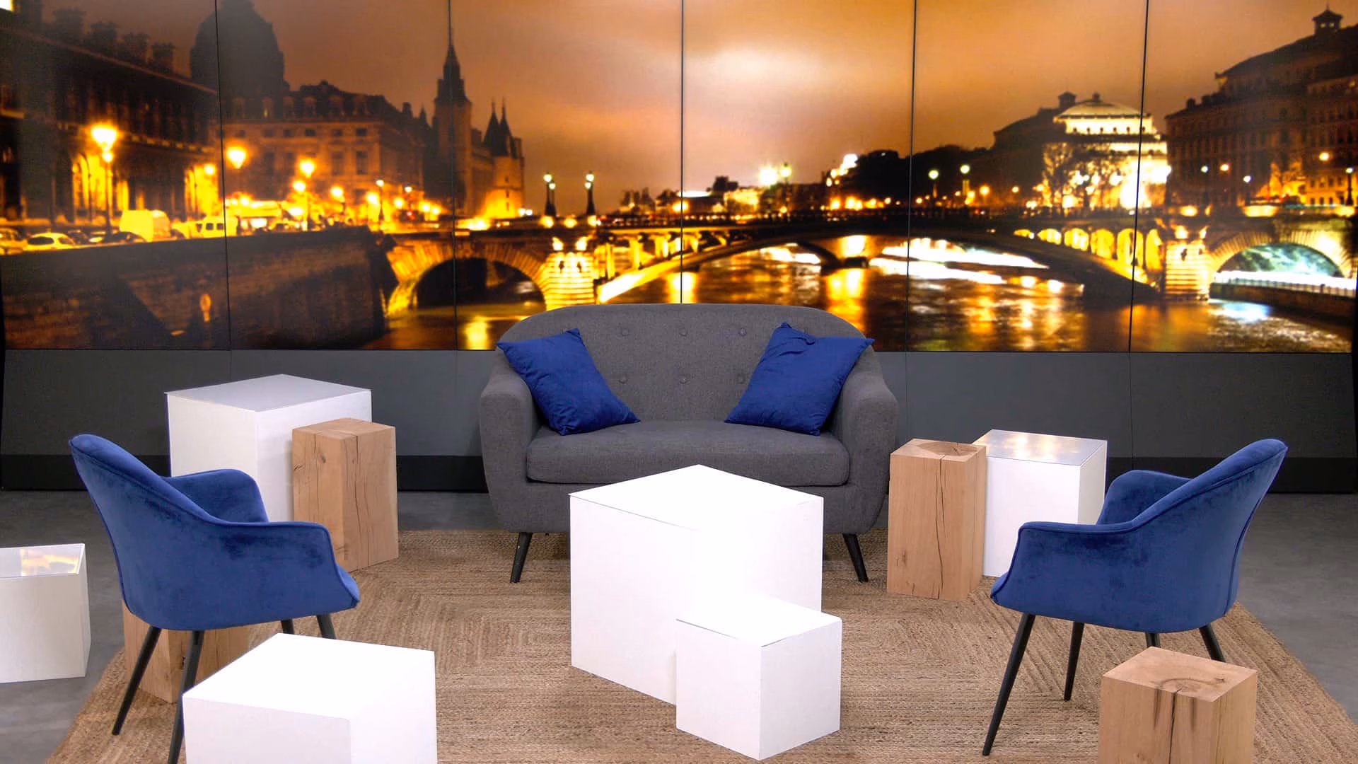 Configuration talk show du plateau TV du Studio Webcast avec fauteuils velours bleu, canapé gris à coussins bleus et fond de décor Paris by night