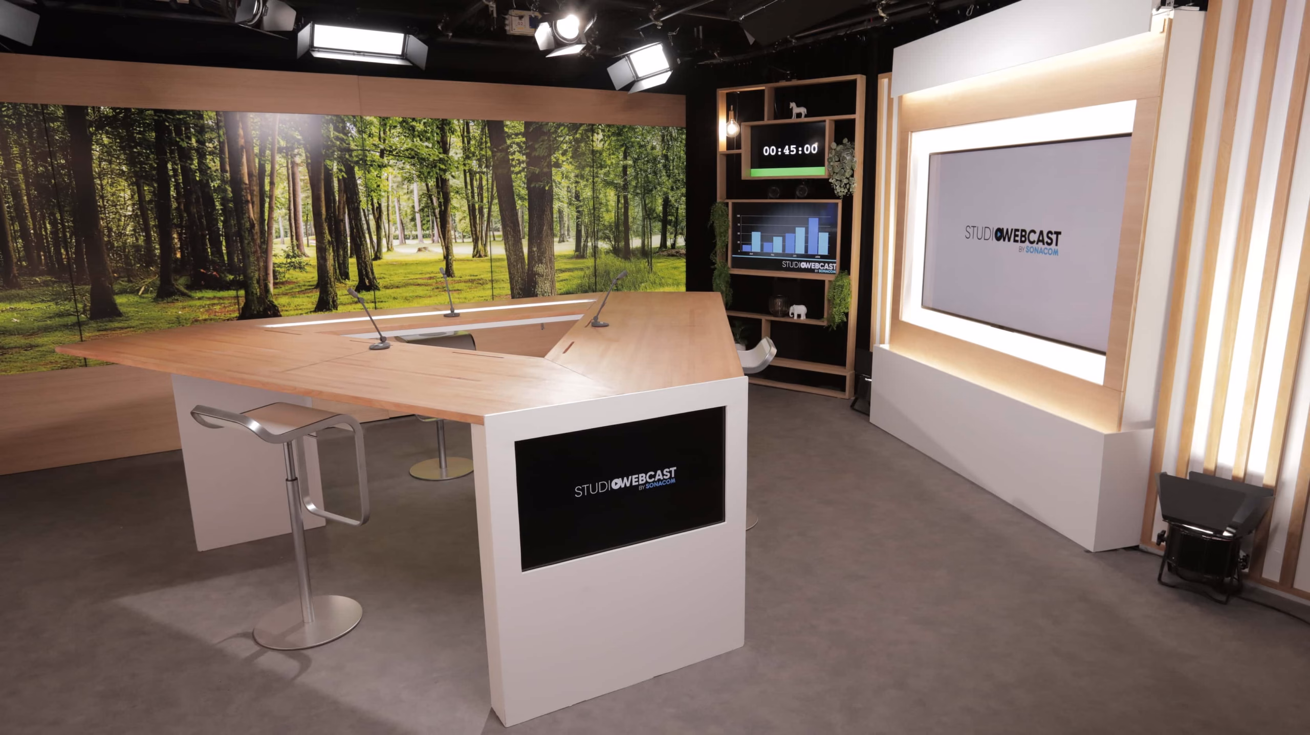 Plateau TV du Studio Webcast en configuration fond de décor forêt verte, bureau hexagonal bois et branding Studio Webcast