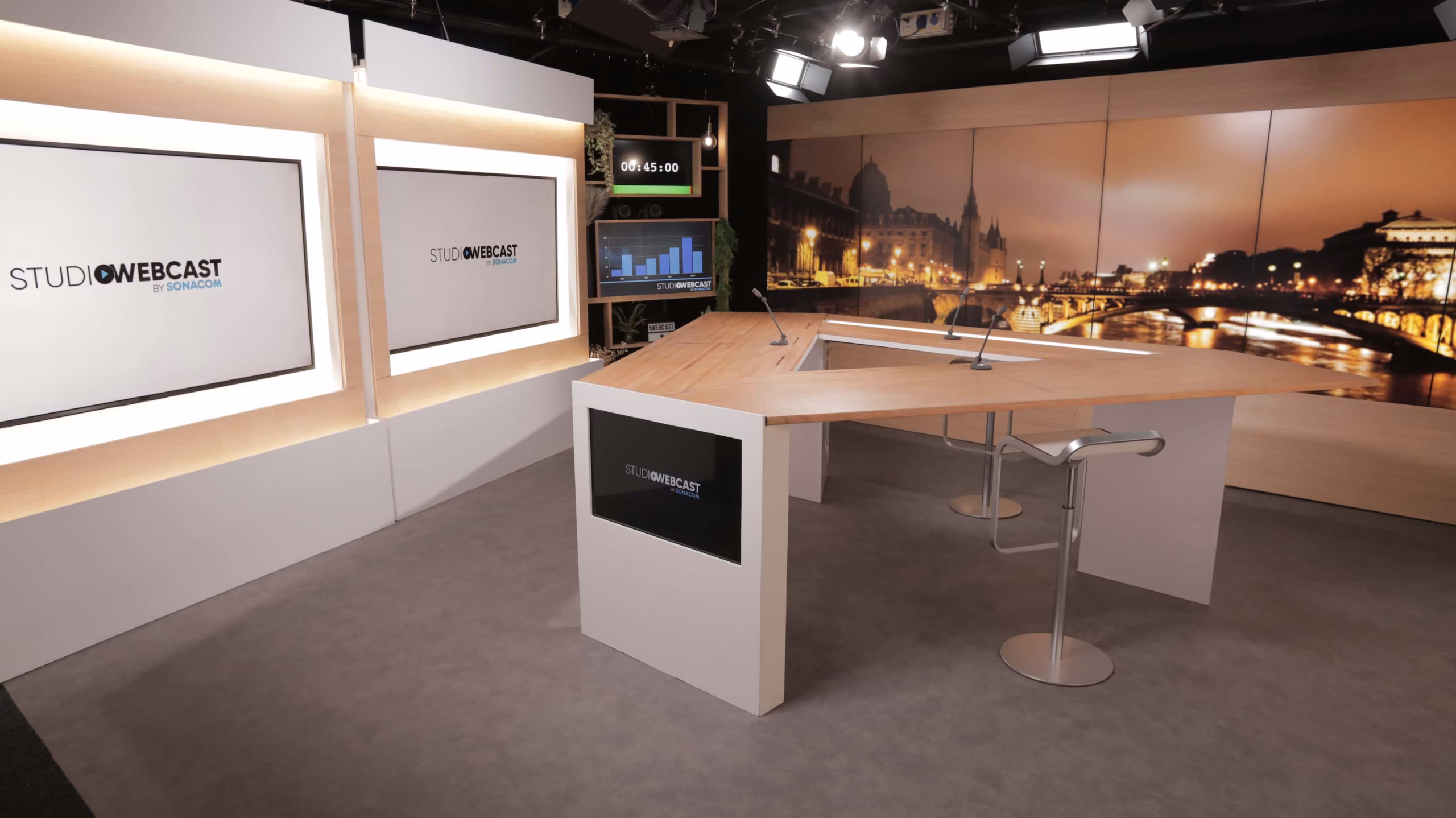 Plateau TV du Studio Webcast avec fond de décor Paris by night sur écran LED, double écran de présentation et bureau hexagonal